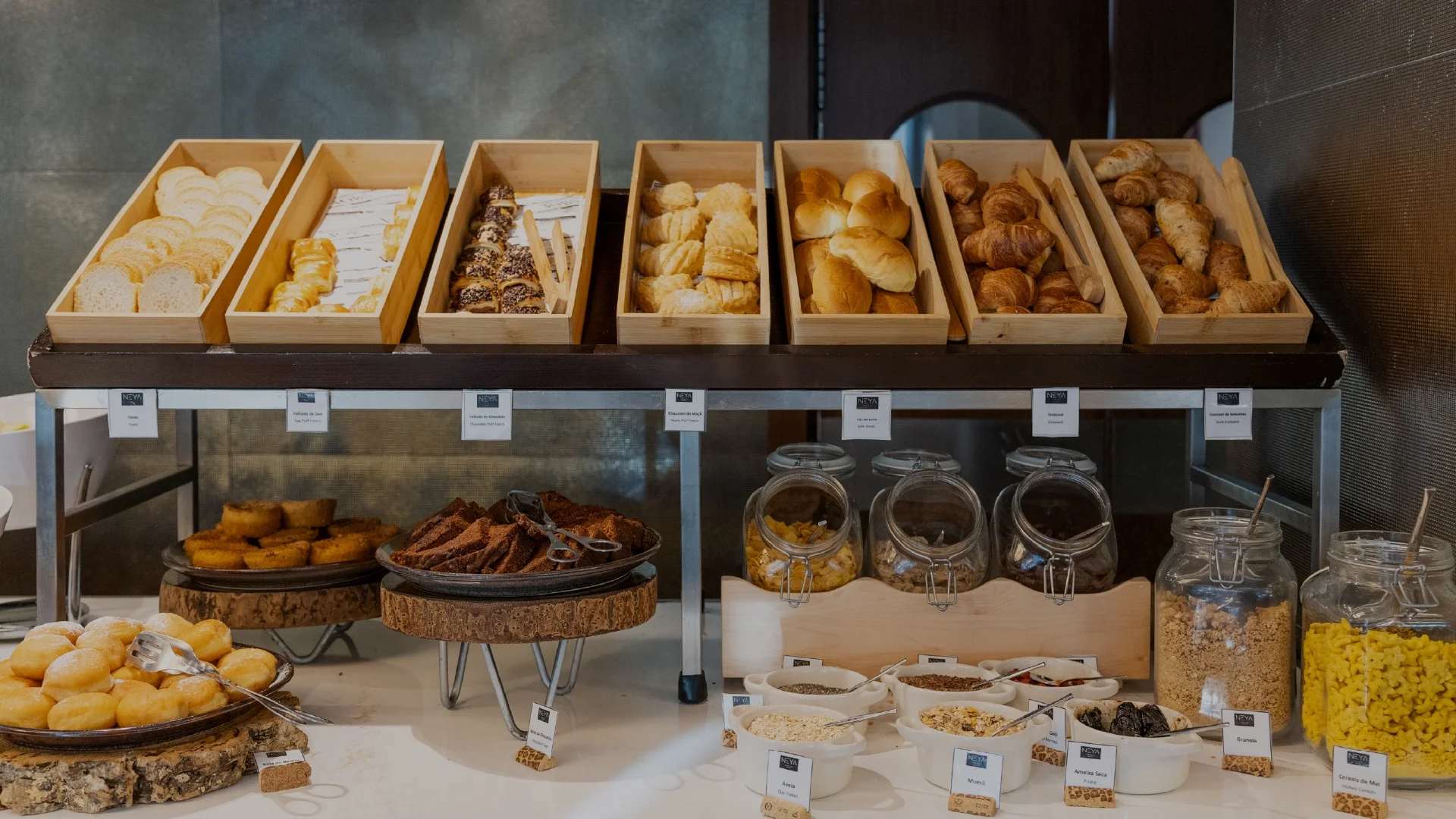 Buffet de pequeno almoço com cestos de produtos de padaria e pastelaria e frascos de vidro comcereais